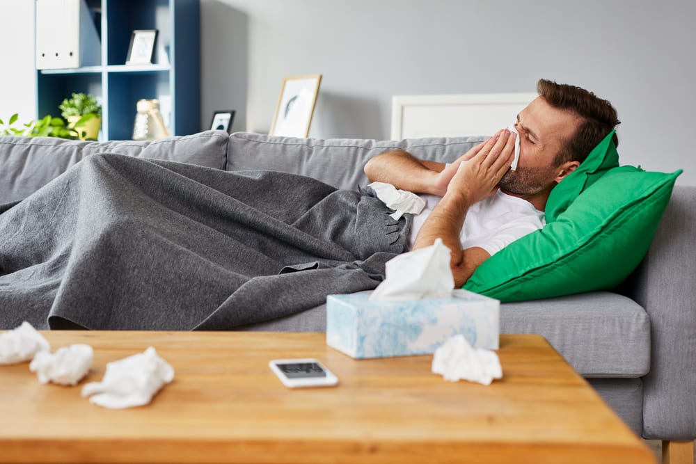 man sick on couch blowing his nose